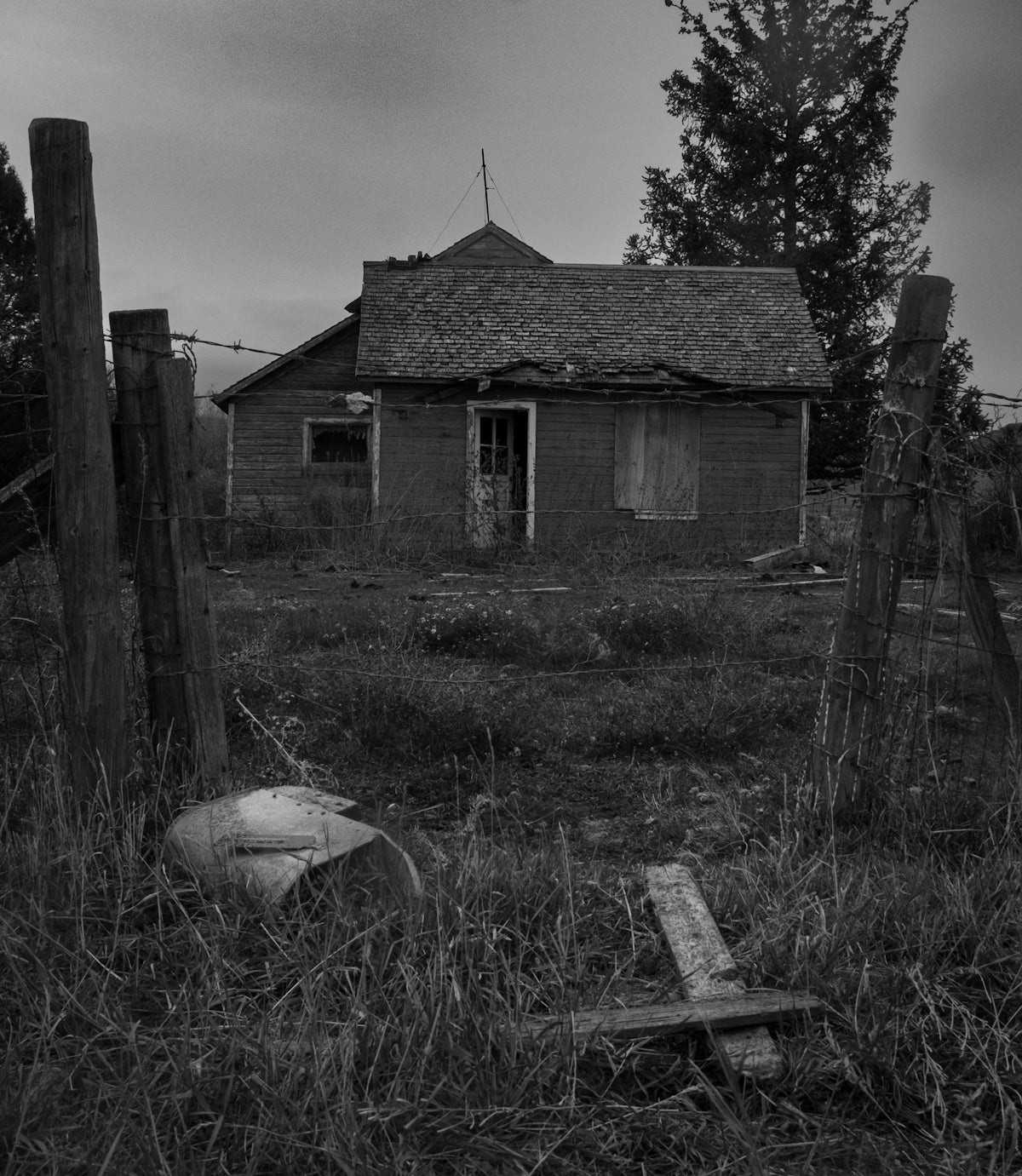 Abandoned rural house with overgrown yard and broken fence