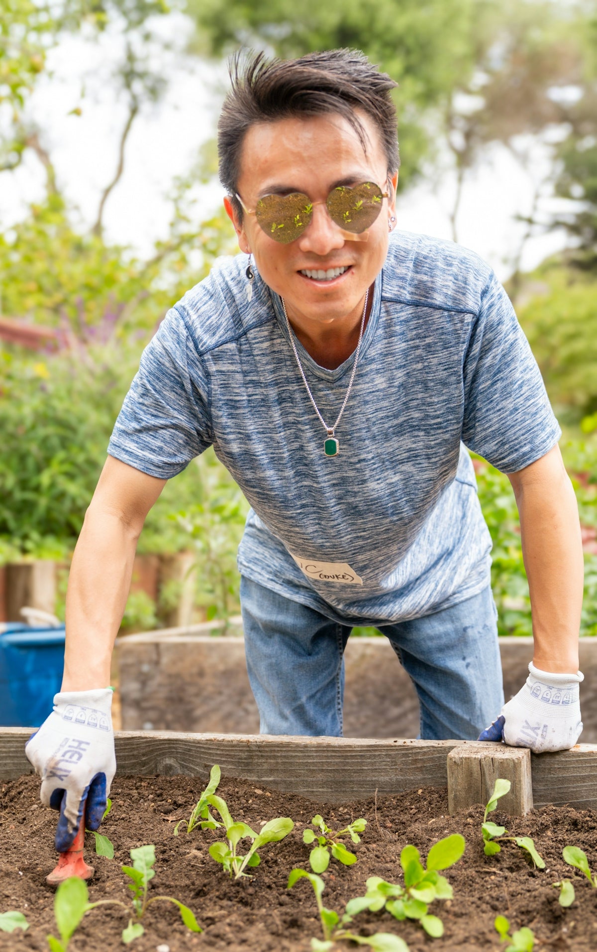 A person in heart-shaped sunglasses gardening in a raised wooden bed