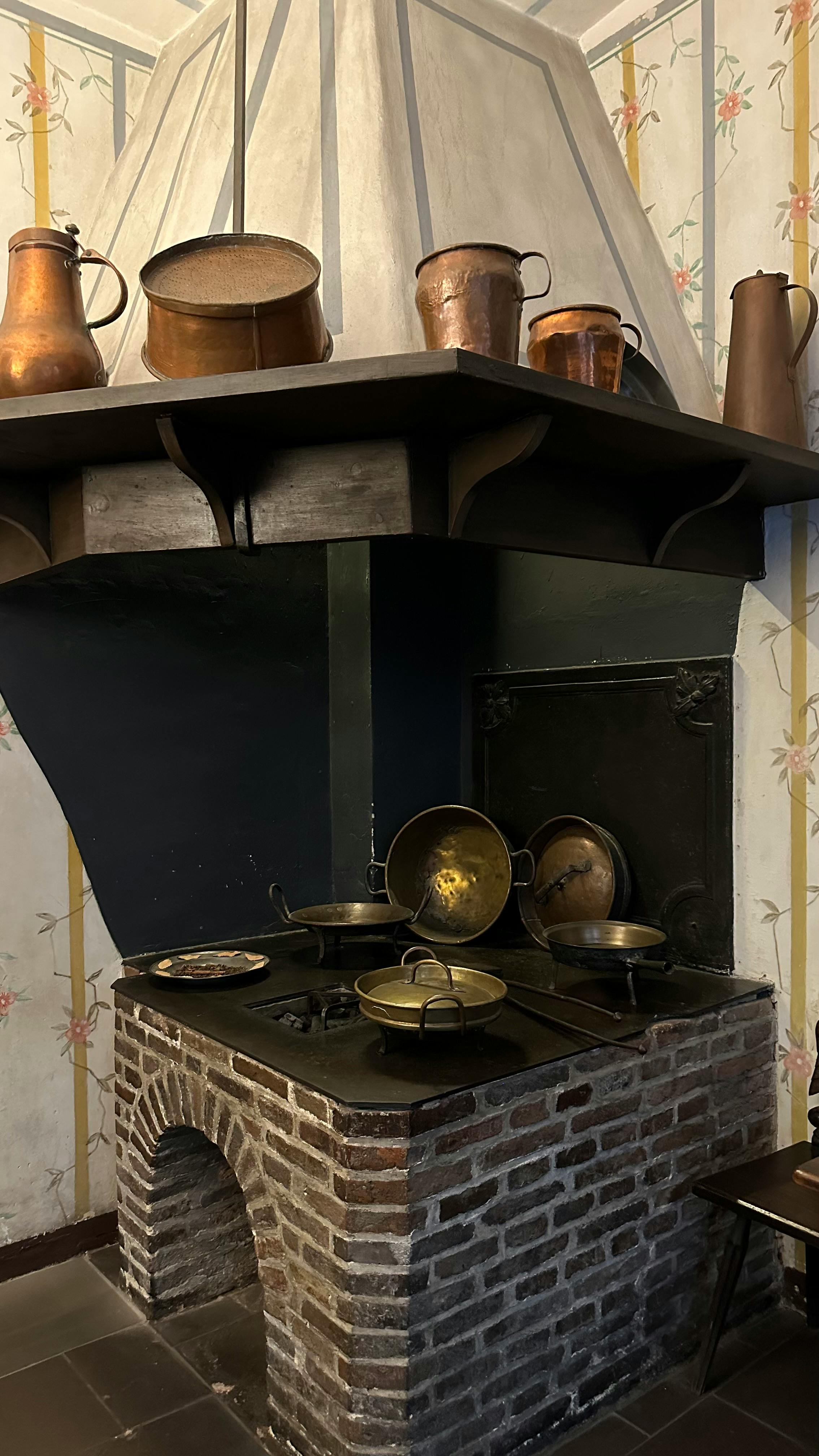 brick oven with cast iron pots and pans covered by a wooden shelf with copper pans 