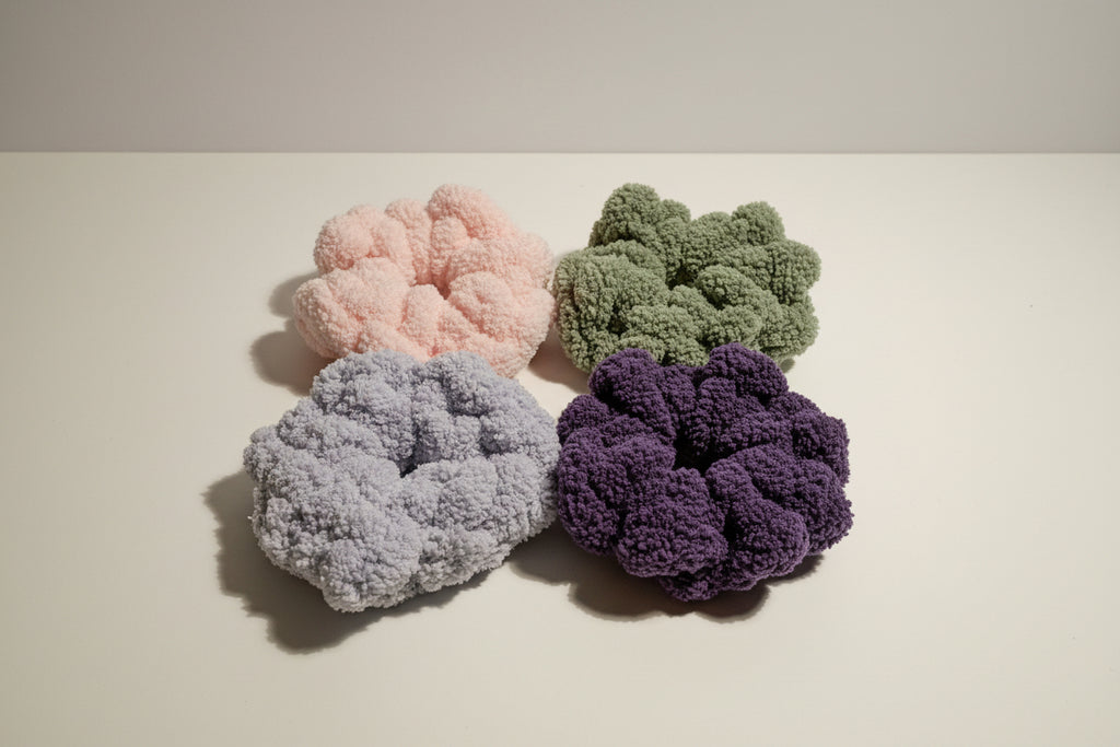 Four textured scrunchies in different colors on a reflective surface.